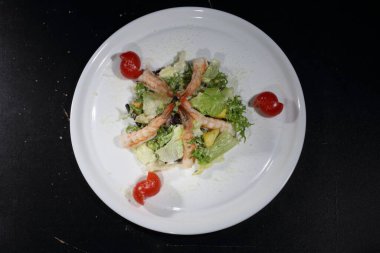Koyu arkaplanda beyaz tabakta karidesli Sezar salatası