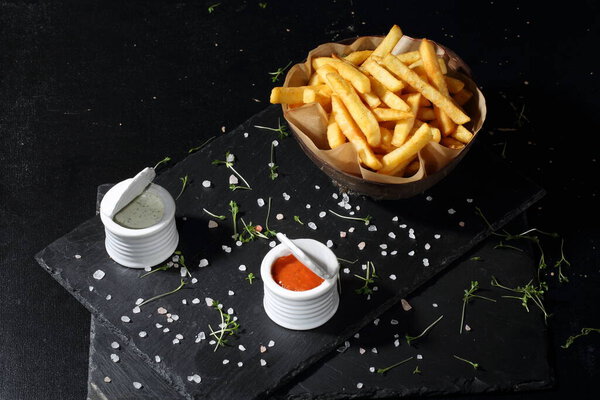 Картофель фри с красным и белым соусом на черном фоне