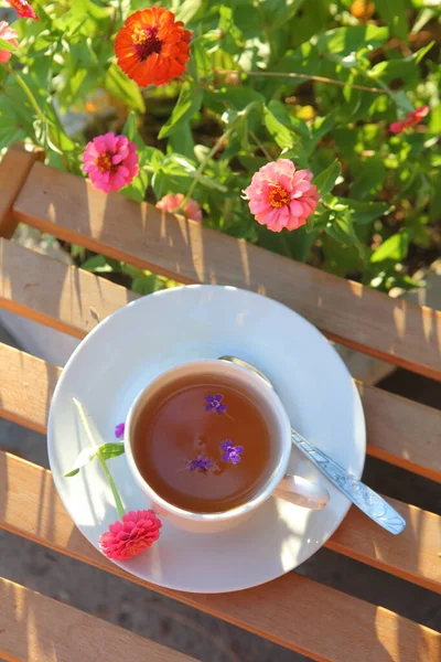 テラスの木のテーブルの上に白いカップと花でお茶 — ストック写真