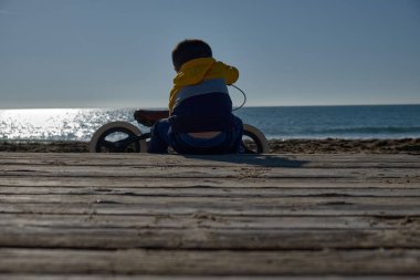Küçük çocuk sahilde bisiklet tamir ediyor.