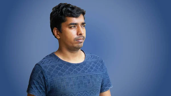 Young handsome man in blue t-shirt and jeans. Indian man standing isolated on dark blue texture.