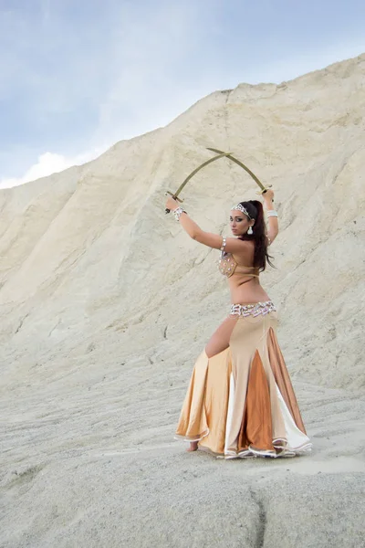 Jovem bela mulher caucasiana dançarina do ventre posando no deserto com espadas, lado de trás Fotos De Bancos De Imagens