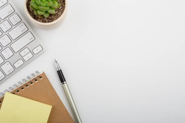 Bilgisayar klavyesi ve diğer ofis malzemeleriyle dolu beyaz ofis masası. Kopyalama alanı olan üst görünüm, düz yatay.
