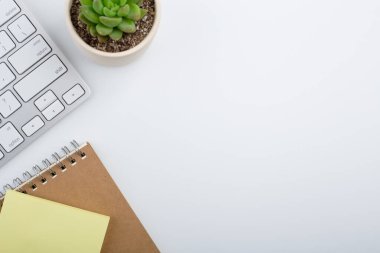 Bilgisayar klavyesi ve diğer ofis malzemeleriyle dolu beyaz ofis masası. Kopyalama alanı olan üst görünüm, düz yatay.