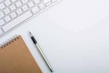 Bilgisayar klavyesi ve diğer ofis malzemeleriyle dolu beyaz ofis masası. Kopyalama alanı olan üst görünüm, düz yatay.