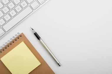 Bilgisayar klavyesi ve diğer ofis malzemeleriyle dolu beyaz ofis masası. Kopyalama alanı olan üst görünüm, düz yatay.
