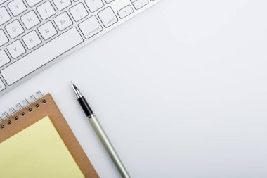 Bilgisayar klavyesi ve diğer ofis malzemeleriyle dolu beyaz ofis masası. Kopyalama alanı olan üst görünüm, düz yatay.