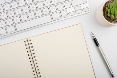 Bilgisayar klavyesi ve diğer ofis malzemeleriyle dolu beyaz ofis masası. Kopyalama alanı olan üst görünüm, düz yatay.