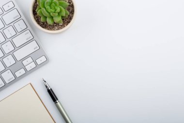 Bilgisayar klavyesi ve diğer ofis malzemeleriyle dolu beyaz ofis masası. Kopyalama alanı olan üst görünüm, düz yatay.