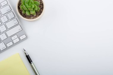 Bilgisayar klavyesi ve diğer ofis malzemeleriyle dolu beyaz ofis masası. Kopyalama alanı olan üst görünüm, düz yatay.