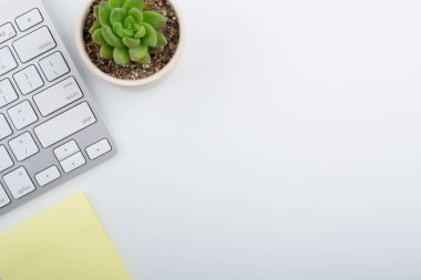 Bilgisayar klavyesi ve diğer ofis malzemeleriyle dolu beyaz ofis masası. Kopyalama alanı olan üst görünüm, düz yatay.