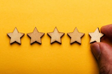 Sarı arka plana beş yıldızlı ahşap bir el koyuyorum. En iyi iş hizmetleri derecelendirme müşteri deneyimi konsepti.