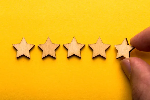 手は黄色の背景に木製の5つ星の形を置く 最高のビジネスサービス評価顧客体験のコンセプト — ストック写真