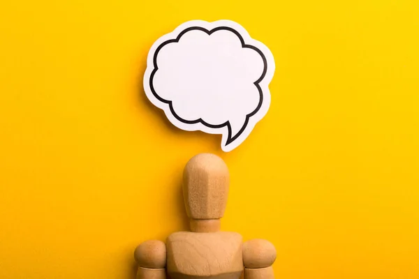 Thinking concept with blank speech bubble and wooden man on yellow background with copy space.