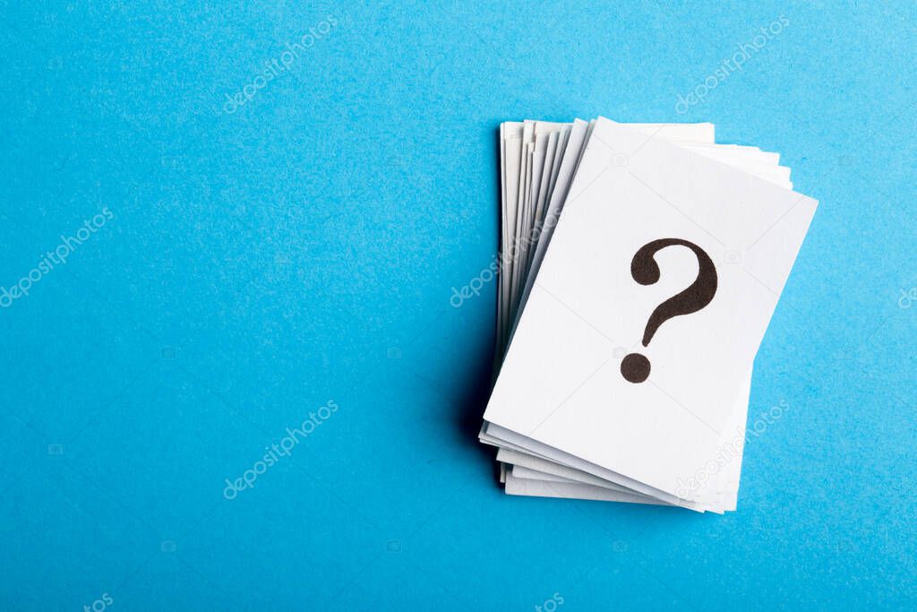 Pile of stacked question marks printed on sheets of white paper or signs arranged to the side on a blue background with copy space in a conceptual image.