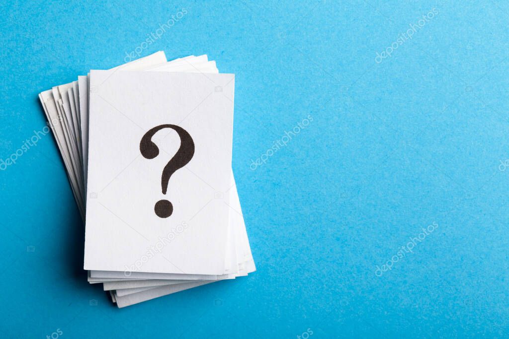 Pile of stacked question marks printed on sheets of white paper or signs arranged to the side on a blue background with copy space in a conceptual image.