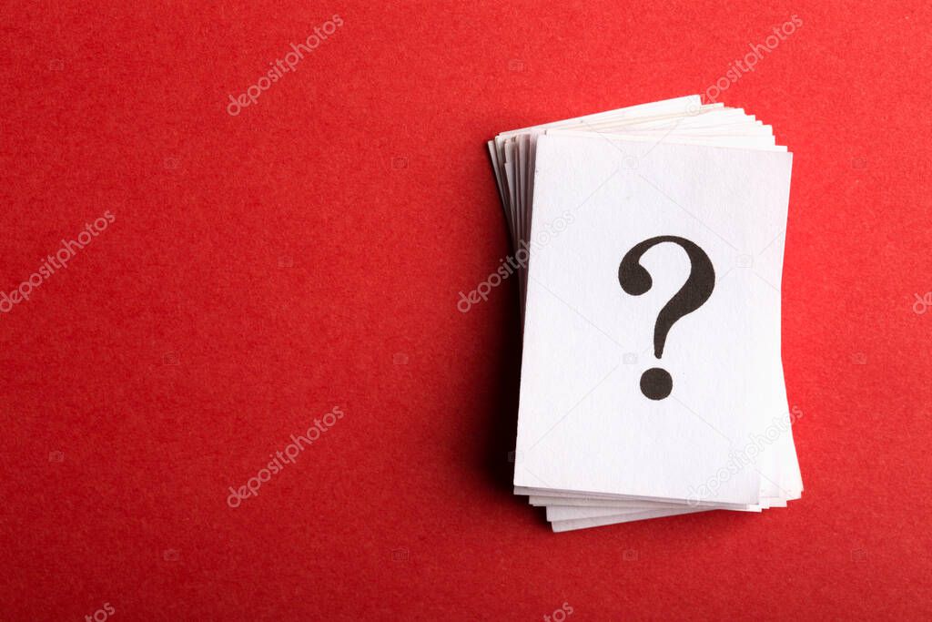 Pile of stacked question marks printed on sheets of white paper or signs arranged to the side on a red background with copy space in a conceptual image.