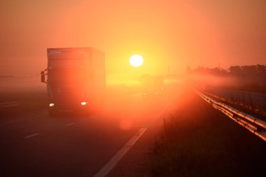Otobanda gün doğumu. Kamyonlar ve arabalar otoyolda gidiyor.