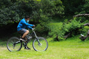 Dışarıda cerrahi maske takmış bisiklet süren genç bir adam.
