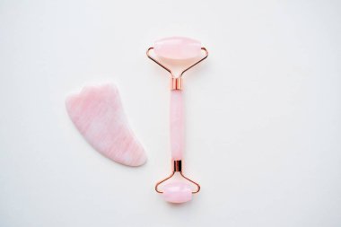 Pembe tekerlekli masaj aleti ve guaj kazıyıcı. Beyaz arka planda gül kuvars yeşim taşı silindiri. Evde reşit olmama, kaldırma ve tonlama tedavisi. Boşluğu kopyala.
