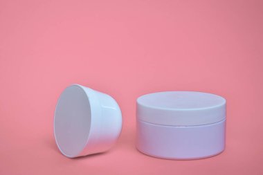 Yuvarlak, beyaz, plastik kozmetik kavanozu, pembe arka planda izole edilmiş düzen..