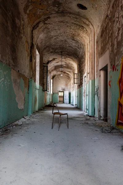 Old abandoned building corridor. Dirty, peeling, blue painted walls. A chair is in the center of the hallway