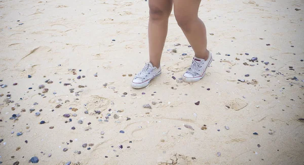 woman leg and old white sneakers on sand sea