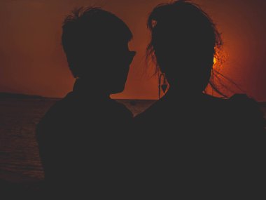 Birkaç siluetin sarılıp güneşin doğuşunu izlediği arka plan.