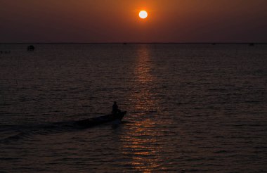 Gün doğumunda ya da batımında denizde yüzen küçük tekneler.