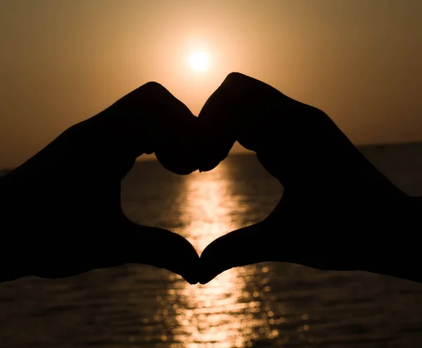 Silhouette hand in heart shape with sunset in the middle
