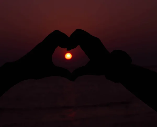 Silhouette hand in heart shape with sunset in the middle