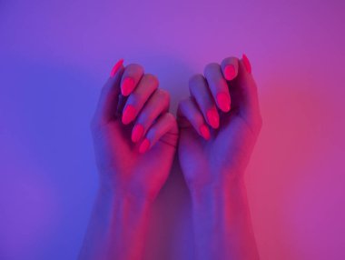 Parlak turuncu renkli güzel manikürlü kadın elleri neon pembe bir ışıkta. Disko biçimi.