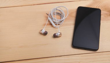Ahşap arka planda akıllı telefon ve kulaklıklar.