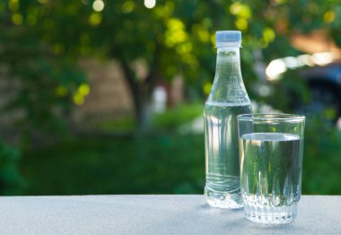 Yeşil doğanın arka planında su şişesi ve cam içmek.