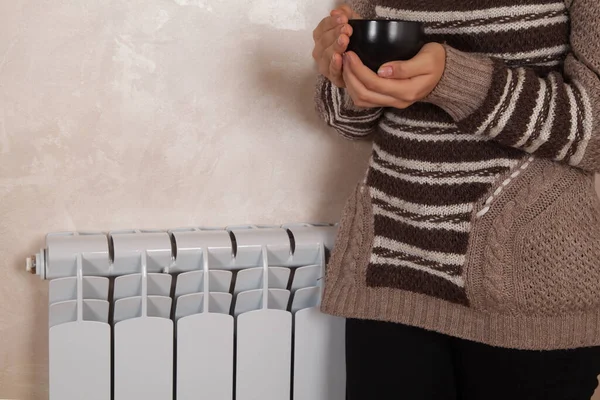 Young woman with tea at home  near electric heater.