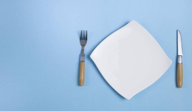 Temiz beyaz tabak bıçak ve çatalla izole edilmiş mavi arka planda..