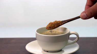 Adding coffee with 3 spoons of organic brown sugar in white ceramic cup hot beverage on wooden table, minimal style morning drink, caffeine boost, warm atmosphere, simple calm refreshment