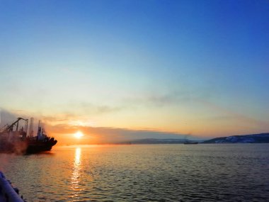 Deniz, gemi ve vincin arka planında gün batımı