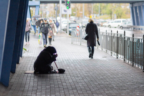 Kiev, Ukraine - October 24, 2018: A beggarly old woman sits on the sidewalk surrounded by passersby