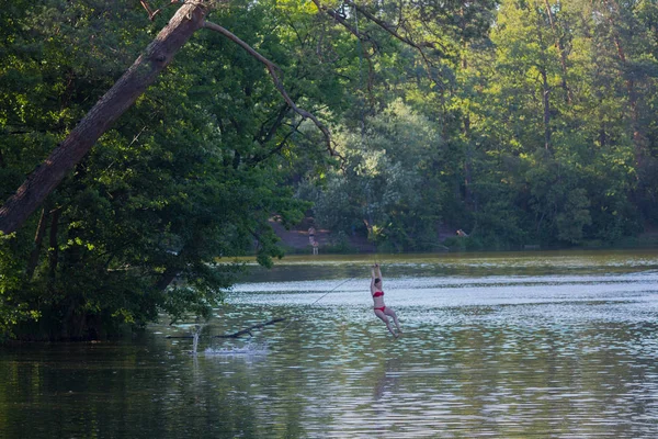 Kiev, Ucrania - 30 de junio de 2017: Niña balanceándose sobre una cuerda y lista para saltar al agua mientras descansa en el lago —  Fotos de Stock