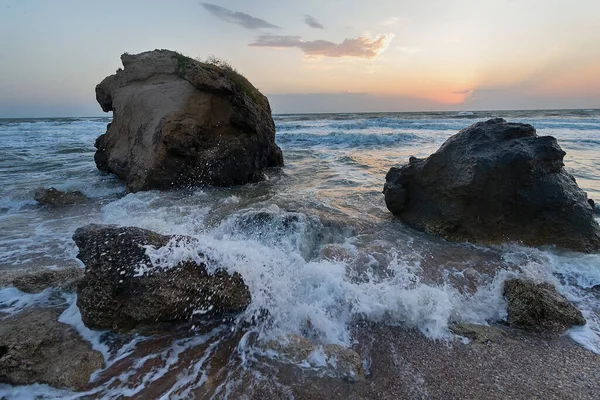 Gün batımında dalgalar plajda kayalara vuruyor. Kırım