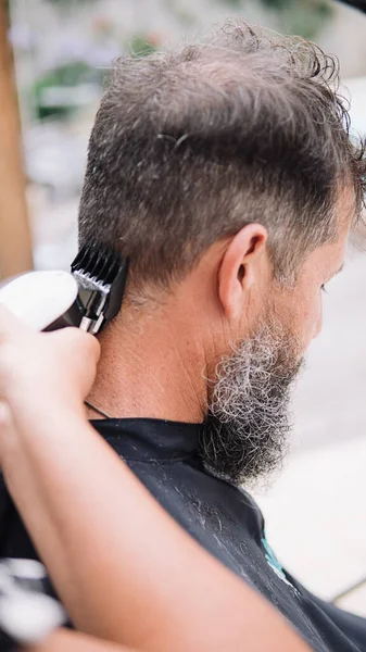 Stock photo of white man with big white and black beard getting a haircut. The hairdresser is using a trimmer.
