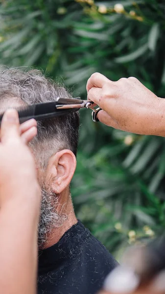 Stock photo of unrecognized man with big white beard getting a haircut. The hairdresser is using a comb and the scissors.