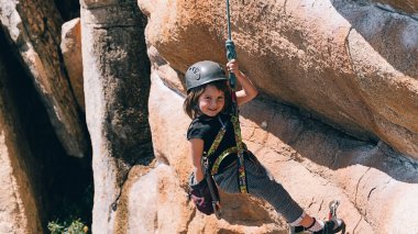 Young girl smiling and having fun while she does rock climbing. She is looking at camera. clipart