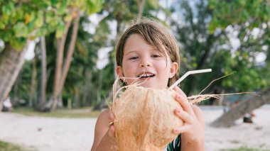 Mutlu bir kızın sahilde eğlenirken ve elinde hindistan cevizi tutarken çekilmiş resmi..