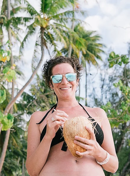 Sahilde eğlenen ve elinde hindistan cevizi tutan neşeli bir kadının stok fotoğrafı..