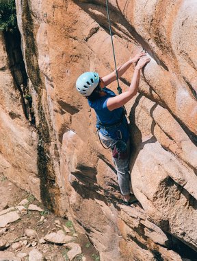 Kask ve emniyet kemeri takan yüzü olmayan kadın dağa tırmanıyor..