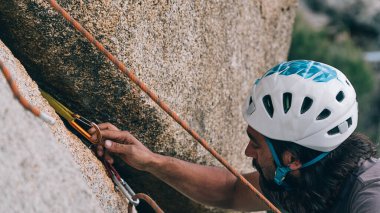 Kask takan ve karabina kullanarak kaya tırmanışı yapan bir adam..