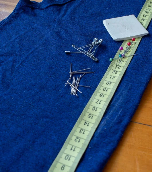 Centimetro sobre una tela azul, con algunos alfileres y una tiza de sastre.