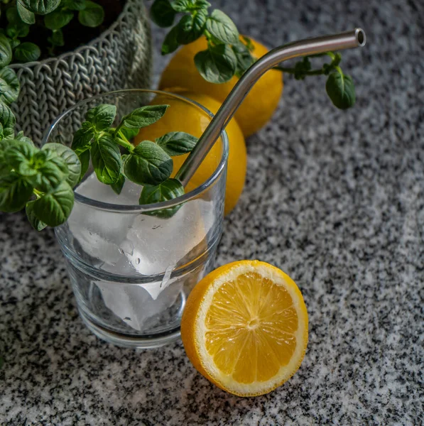 Vaso de vidrio con cubos de hielo, limones y menta  sobre una mesada, concepto de frescura.